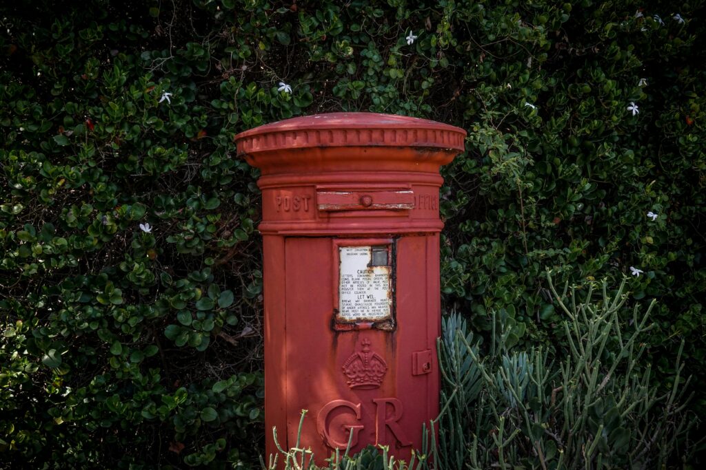 A classic red postbox surrounded by lush green bushes, capturing vintage charm.
