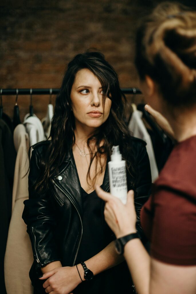 Two women discuss fashion in an urban boutique setting, one holding a product.