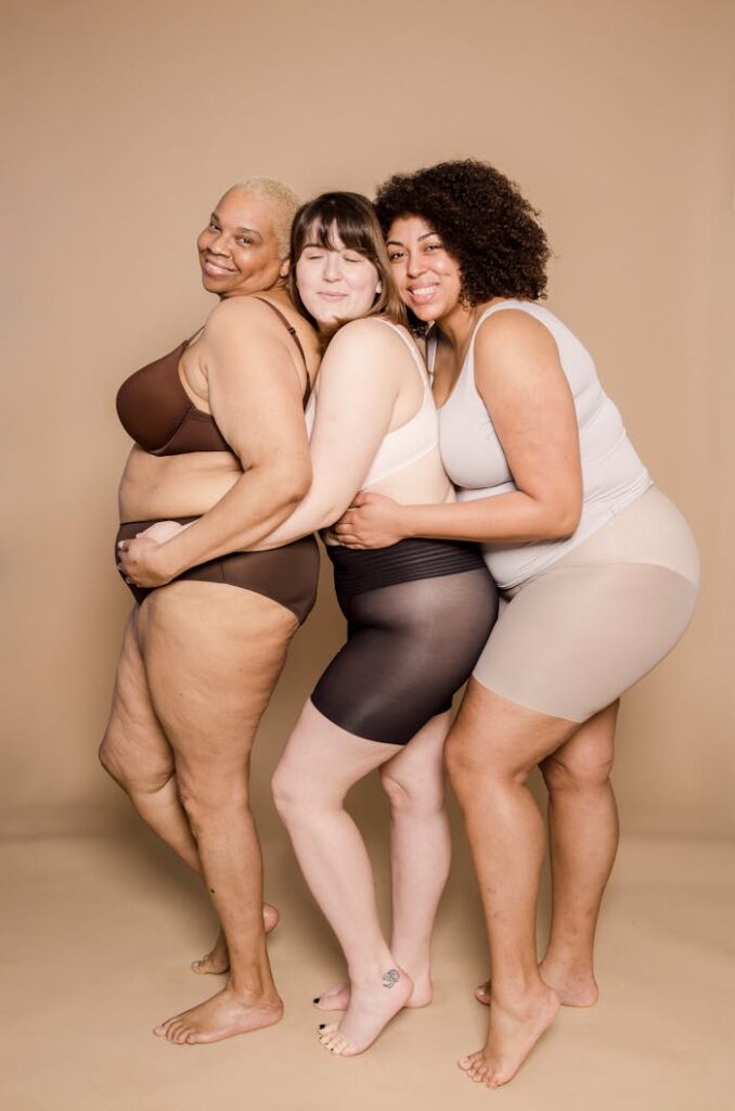 Three diverse plus-size women embracing in studio, celebrating body positivity.